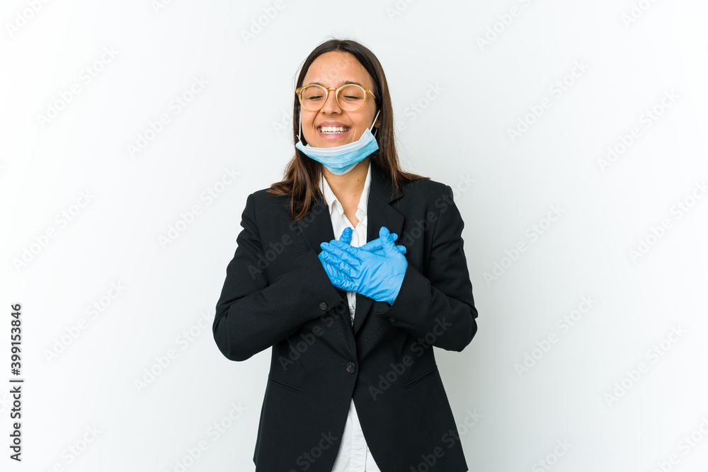 Young business latin woman wearing a mask to protect from covid isolated on white background laughing keeping hands on heart, concept of happiness. Young business latin woman wearing a mask to protect from covid isolated on white background laughing keeping hands on heart, concept of happiness.