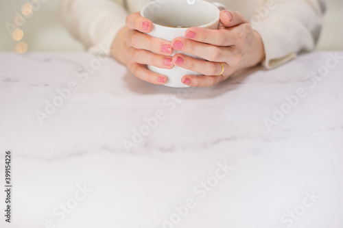 白いマグカップに入った飲み物を飲む女性の手元。