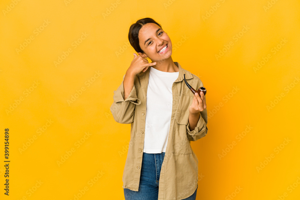 Young hispanic woman holding a smoking pipe showing a mobile phone call gesture with fingers. Young hispanic woman holding a smoking pipe showing a mobile phone call gesture with fingers.