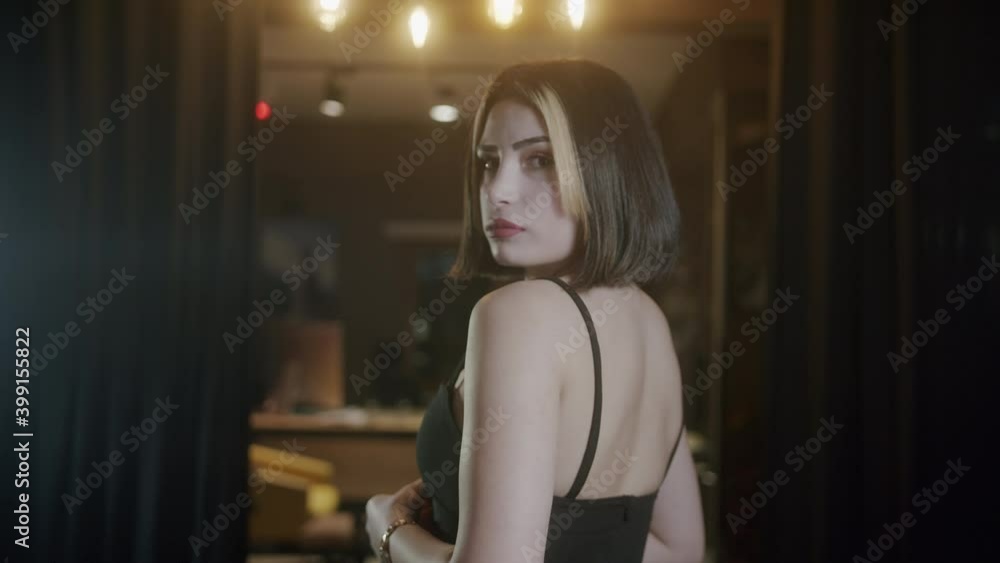 Young beautiful and attractive woman with short hair in a black dress turns her back and poses for the camera. Young beautiful and attractive woman with short hair in a black dress turns her back and poses for the camera.