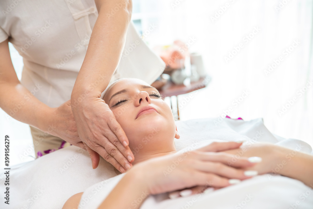 Fototapeta premium Young beautiful Caucasian woman lying on spa bed get facial massage treatment with aroma essential oil skincare from massage therapist at beauty salon. Wellness body massage and face spa concept