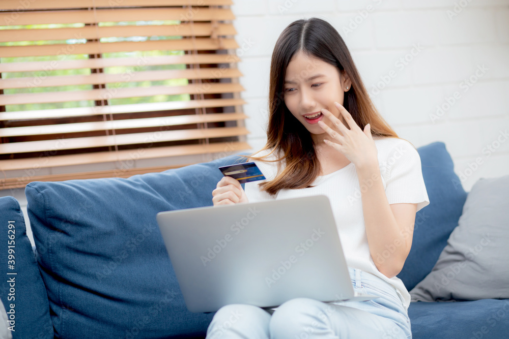 Young asian woman sit on sofa using laptop computer shopping online with credit card buy to internet and surprise, happy girl payment with e-business on couch, success and excited, business concept.