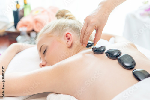 Young beautiful Caucasian woman lying on spa bed get back massage treatment with essential oil skincare and hot stone from massage therapist at beauty salon. Wellness body massage and spa concept.