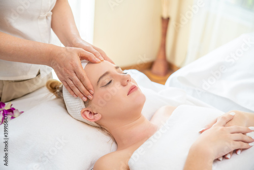 Young beautiful Caucasian woman lying on spa bed get facial massage treatment with aroma essential oil skincare from massage therapist at beauty salon. Wellness body massage and face spa concept