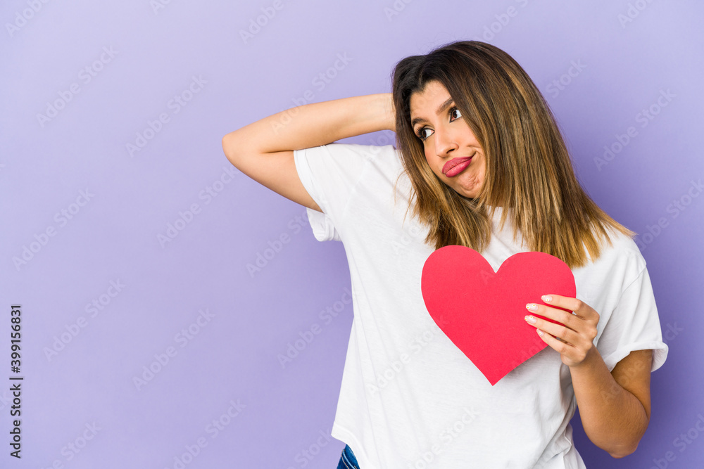 Young indian woman holding a valentines day heart isolated touching back of head, thinking and making a choice. Young indian woman holding a valentines day heart isolated touching back of head, thinking and making a choice.
