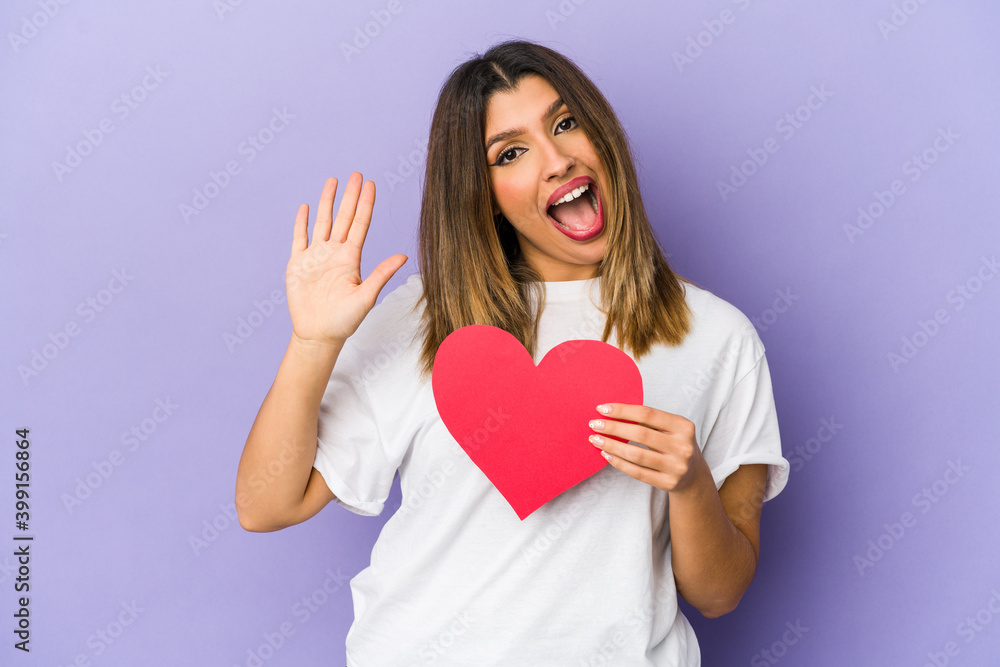 Young indian woman holding a valentines day heart isolated smiling cheerful showing number five with fingers. Young indian woman holding a valentines day heart isolated smiling cheerful showing number five with fingers.