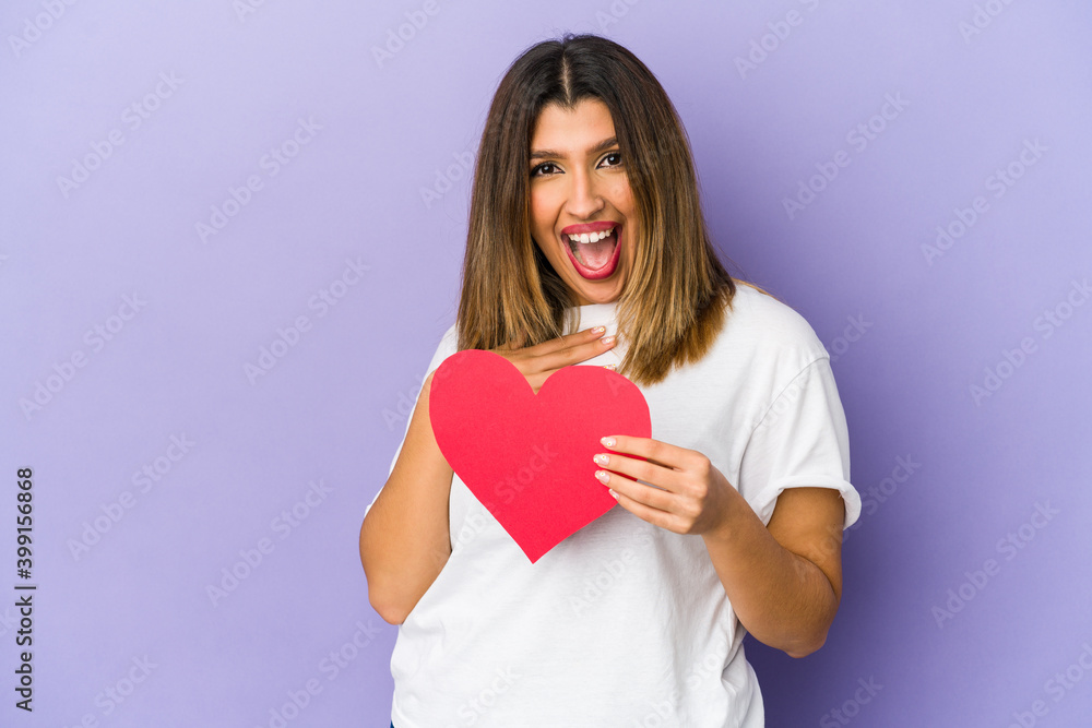 Young indian woman holding a valentines day heart isolated laughs out loudly keeping hand on chest. Young indian woman holding a valentines day heart isolated laughs out loudly keeping hand on chest.