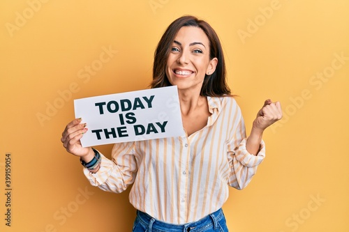 Young brunette woman holding today is the day screaming proud, celebrating victory and success very excited with raised arm photo