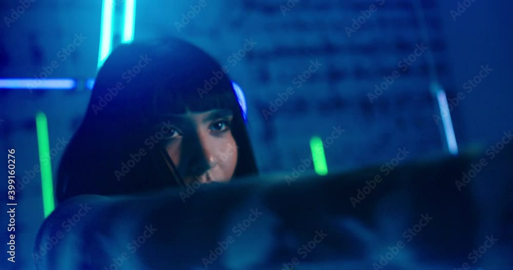 Camera focuses at cyberpunk young woman with short dark hair dancing to electronic music against futuristic neon lights closeup Camera focuses at cyberpunk young woman with short dark hair dancing to electronic music against futuristic neon lights closeup