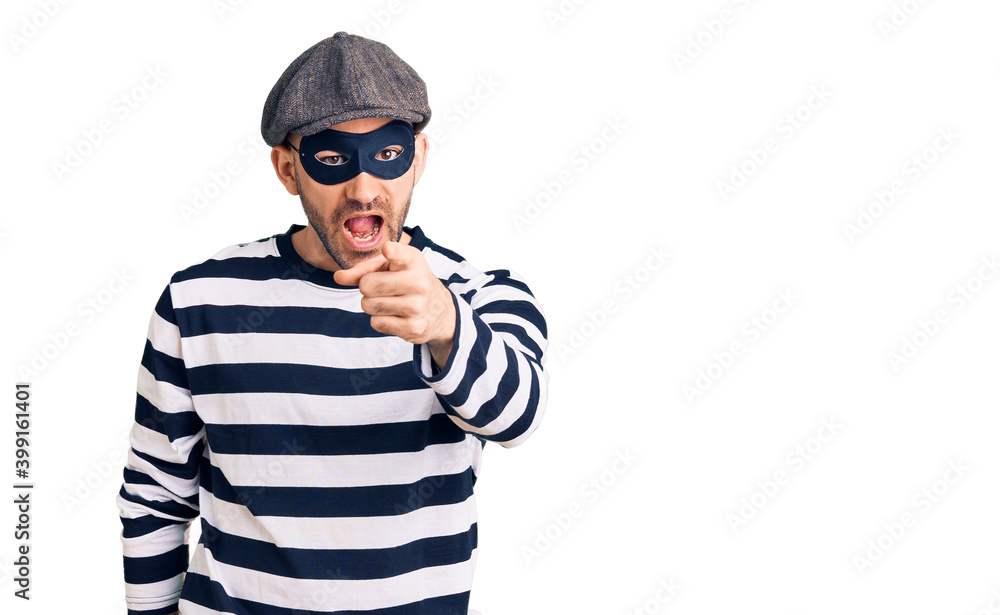 Young handsome man wearing burglar mask pointing displeased and frustrated to the camera, angry and furious with you Young handsome man wearing burglar mask pointing displeased and frustrated to the camera, angry and furious with you