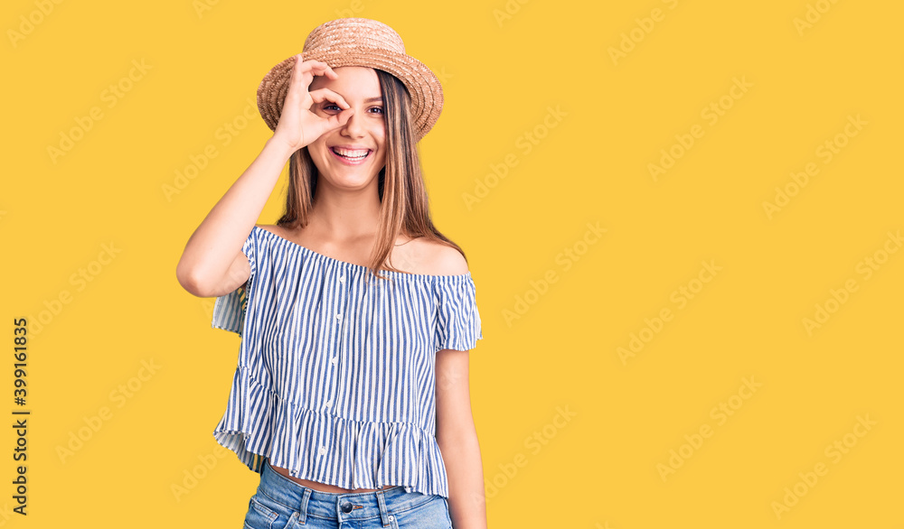 Young beautiful girl wearing hat and t shirt doing ok gesture with hand smiling, eye looking through fingers with happy face. Young beautiful girl wearing hat and t shirt doing ok gesture with hand smiling, eye looking through fingers with happy face.