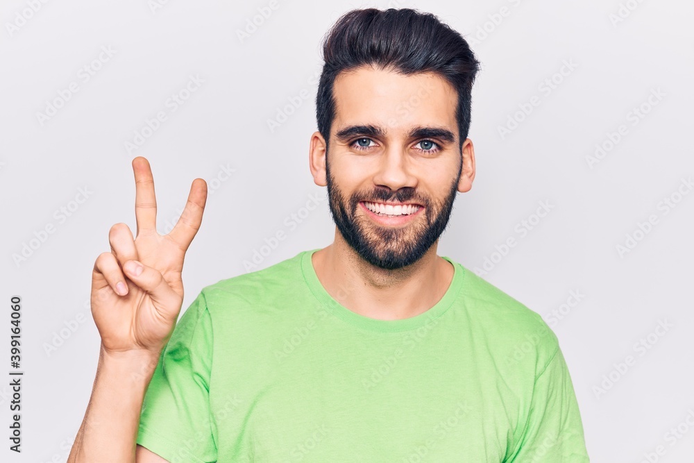 Young handsome man with beard wearing casual t-shirt smiling with happy face winking at the camera doing victory sign. number two. Young handsome man with beard wearing casual t-shirt smiling with happy face winking at the camera doing victory sign. number two.