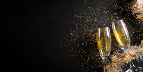 Christmas and New Year holidays background concept made from champagne glasses with golden glitter on black wooden background.