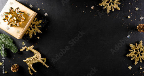Christmas and new year background concept. Top view of Christmas gift box, spruce branches, pine cones and snowflake on black wooden background.
