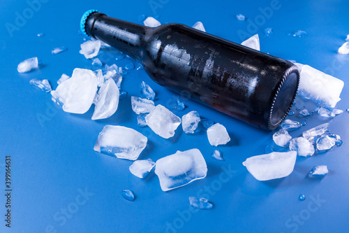 Bottle of beer with ice on blue background