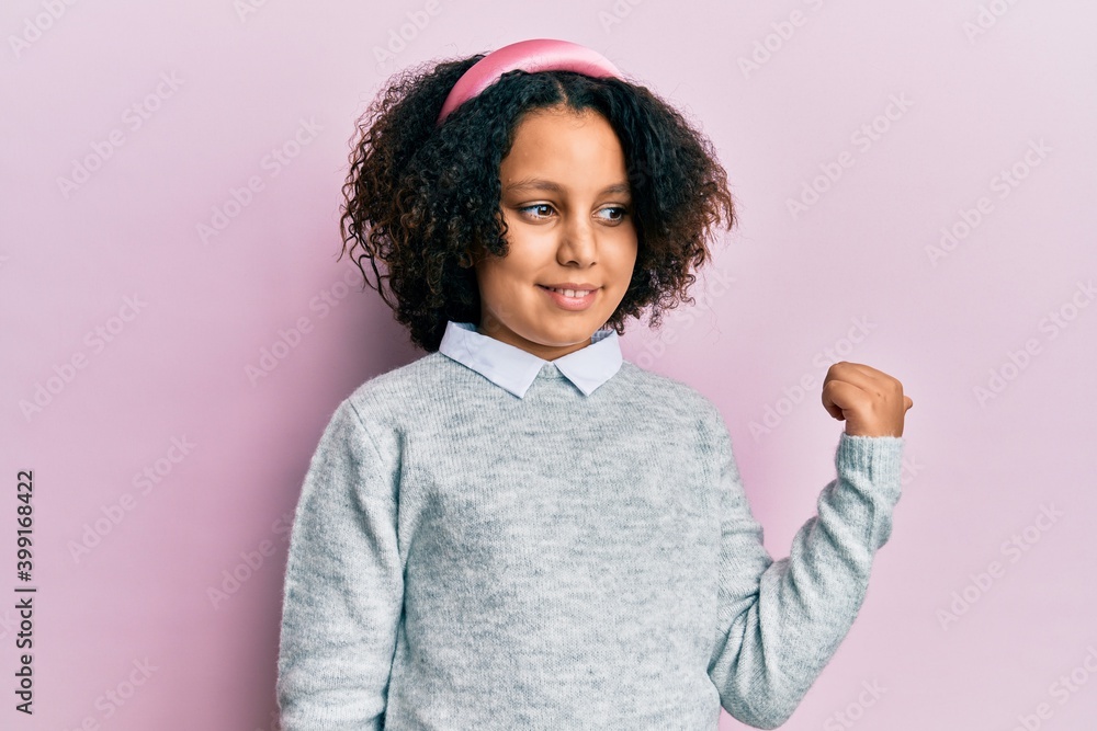 Young little girl with afro hair wearing casual clothes smiling with happy face looking and pointing to the side with thumb up. Young little girl with afro hair wearing casual clothes smiling with happy face looking and pointing to the side with thumb up.