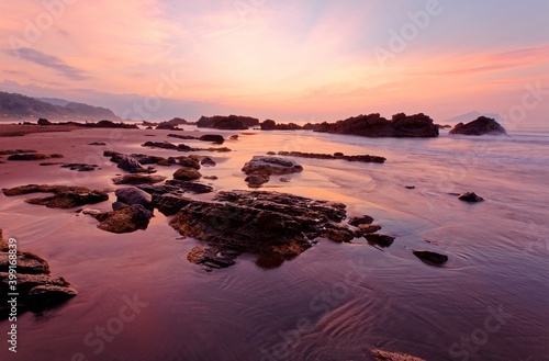 Sunrise scenery of a beautiful rocky beach on northern coast of Taiwan with an island on distant horizon under dramatic dawning sky & golden sunlight reflecting on the seawater (Long Exposure Effect)