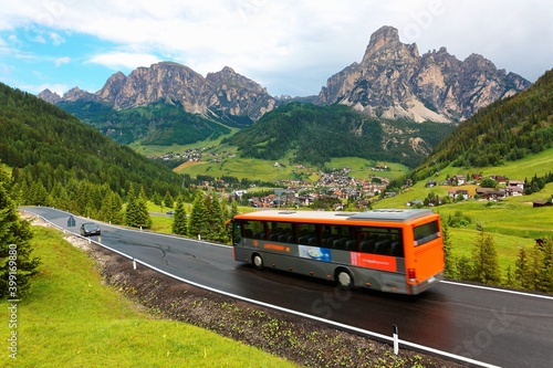 Cars & buses traveling on a scenic highway thru a green grassy valley with villages on the hillside of rugged mountains after a summer shower in Corvara, Badia, Dolomites, Trentino, South Tyrol, Italy
