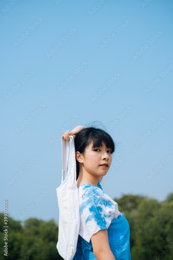 Asian woman wear blue dress with white bag behind the back. Asian woman wear blue dress with white bag behind the back.