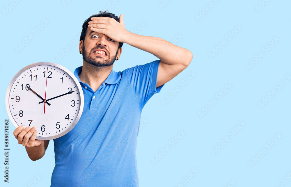 Young hispanic man holding big clock stressed and frustrated with hand on head, surprised and angry face Young hispanic man holding big clock stressed and frustrated with hand on head, surprised and angry face