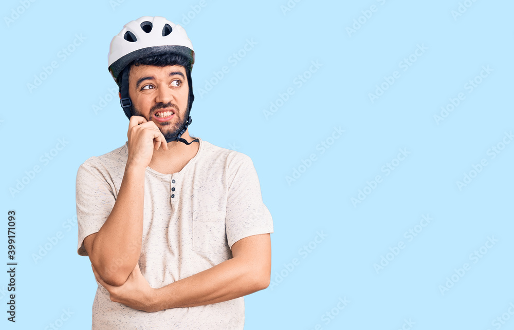 Young hispanic man wearing bike helmet serious face thinking about question with hand on chin, thoughtful about confusing idea Young hispanic man wearing bike helmet serious face thinking about question with hand on chin, thoughtful about confusing idea