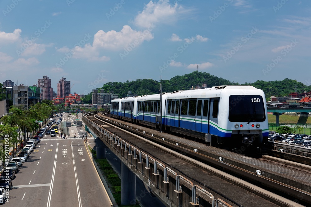 Naklejka premium View of a train traveling on elevated rails of Taipei Metro System in suburban area under blue clear sky ~ View of railways in Mucha, Taipei, the capital city of Taiwan, on a beautiful sunny day