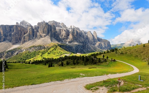 Summer scenery of majestic Sella Mountains & hiking trails winding in the green grassy valley on a cloudy sunny day in Pass Gardena, Dolomites, Bolzano, Trentino, South Tyrol, Italy