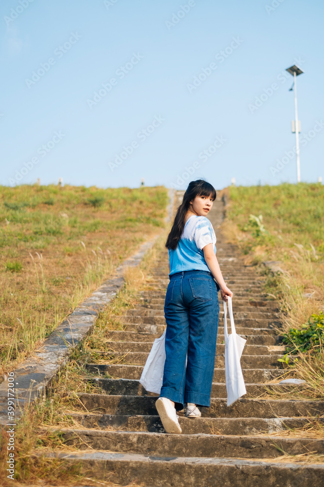 Back view - Asian woman wear blue dress with white canvas walking up stair. Back view - Asian woman wear blue dress with white canvas walking up stair.