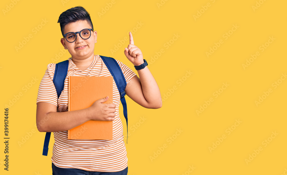 Little boy kid wearing student backpack holding books surprised with an idea or question pointing finger with happy face, number one Little boy kid wearing student backpack holding books surprised with an idea or question pointing finger with happy face, number one