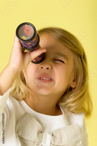 A little girl looks into a telescope or in a kaleidoscope.