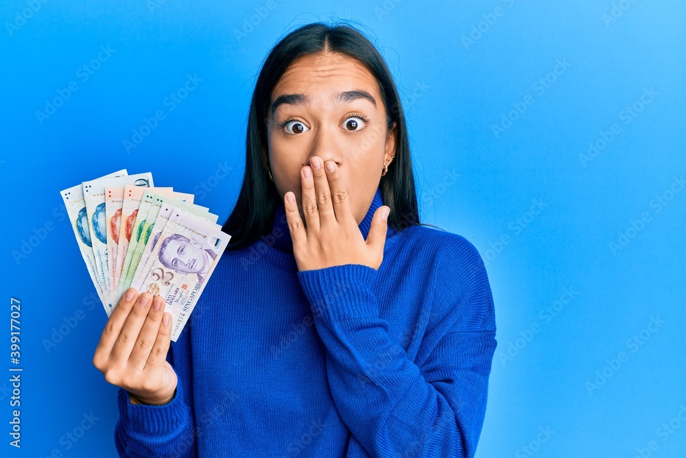 Young asian woman holding singapore dollars banknotes covering mouth with hand, shocked and afraid for mistake. surprised expression Young asian woman holding singapore dollars banknotes covering mouth with hand, shocked and afraid for mistake. surprised expression