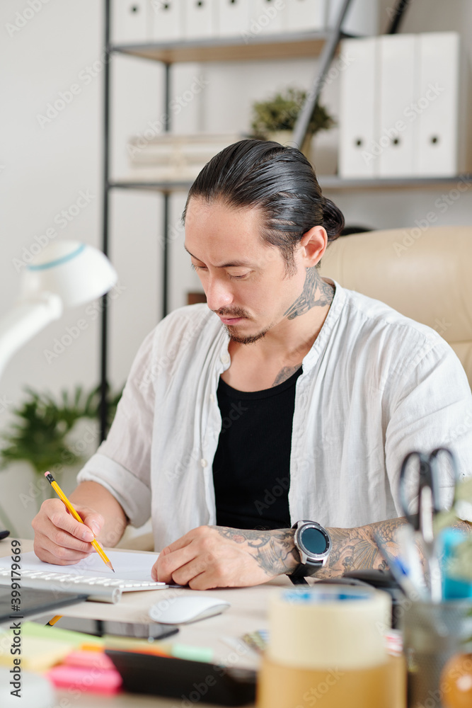 Graphic designer drawing sketch of logo for client when sitting at desk in his home office Graphic designer drawing sketch of logo for client when sitting at desk in his home office