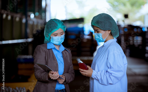 Portrait worker of science in bottle beverage factory wearing safety uniform ,face mask discussion and working to check quality of drink Basil seed produce on conveyer before distribution to market. 