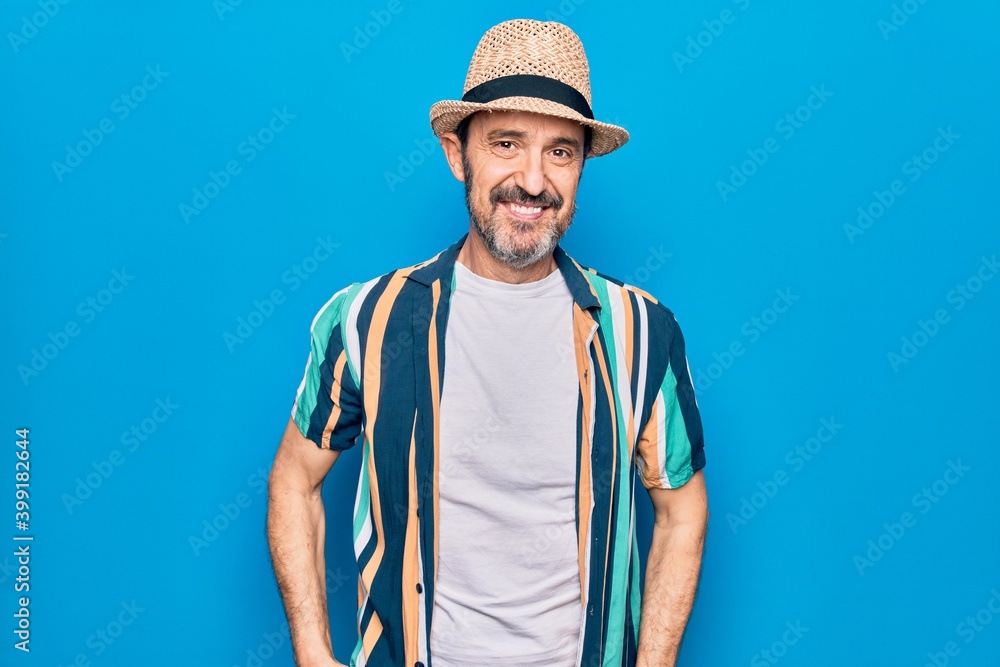 Middle age handsome tourist man on vacation wearing shirt and hat over blue background with a happy and cool smile on face. Lucky person. Middle age handsome tourist man on vacation wearing shirt and hat over blue background with a happy and cool smile on face. Lucky person.