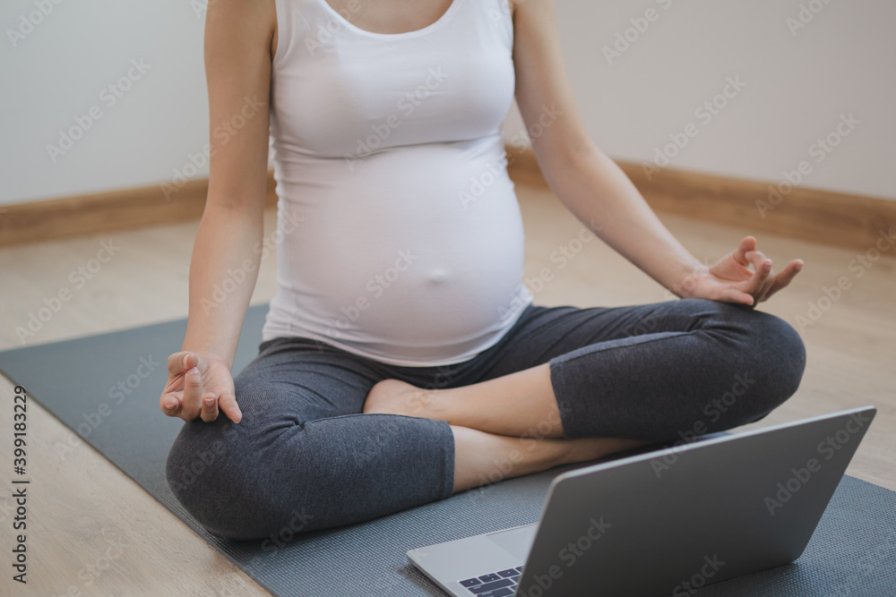 Calm pose young asian pregnant woman meditating in lotus position ,practicing yoga for maternity on laptop computer at home.