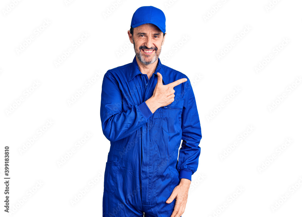 Middle age handsome man wearing mechanic uniform cheerful with a smile on face pointing with hand and finger up to the side with happy and natural expression