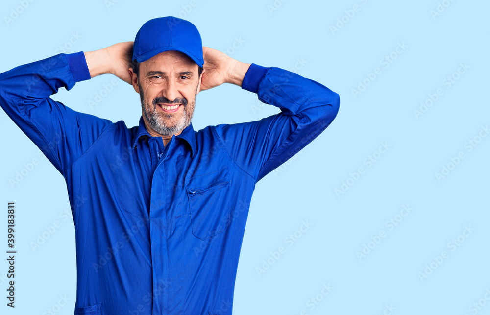 Middle age handsome man wearing mechanic uniform relaxing and stretching, arms and hands behind head and neck smiling happy Middle age handsome man wearing mechanic uniform relaxing and stretching, arms and hands behind head and neck smiling happy