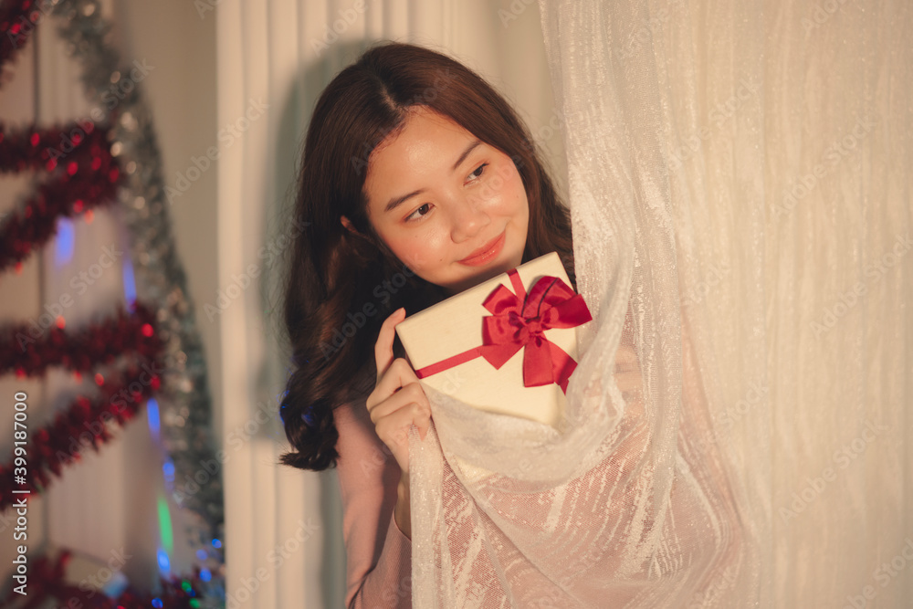 Beauty asian woman black hair holding christmas gift box behind white curtain. Beauty asian woman black hair holding christmas gift box behind white curtain.