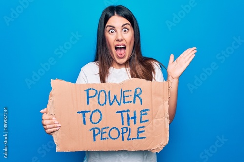 Young woman asking for social movement holding banner with power to the people message celebrating achievement with happy smile and winner expression with raised hand