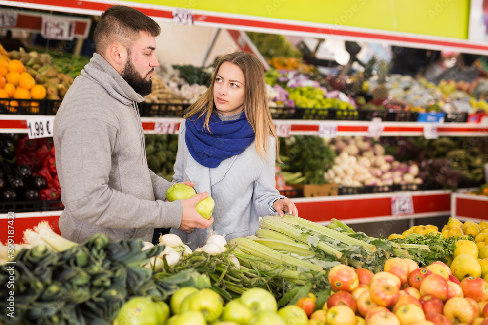 Friendly couple examining apples in grocery shop. High quality photo