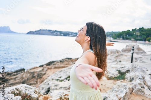 Young beautiful woman on back view breathing with arms open at the beach