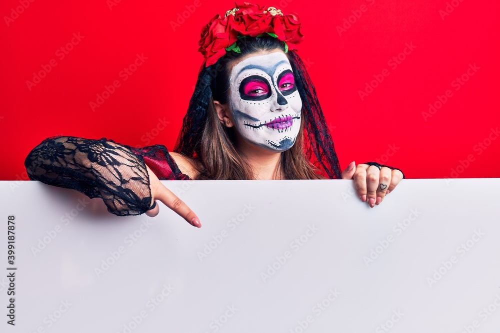 Young woman wearing day of the dead costume holding blank empty banner smiling happy pointing with hand and finger