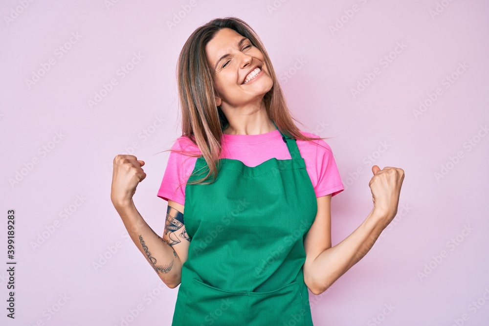 Beautiful caucasian woman wearing professional apron very happy and excited doing winner gesture with arms raised, smiling and screaming for success. celebration concept. Beautiful caucasian woman wearing professional apron very happy and excited doing winner gesture with arms raised, smiling and screaming for success. celebration concept.