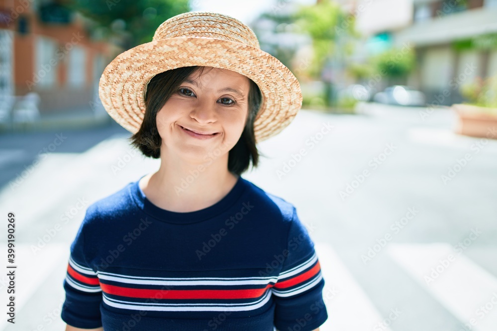 Beautiful brunette woman with down syndrome wearing a summer hat at the town on a sunny day