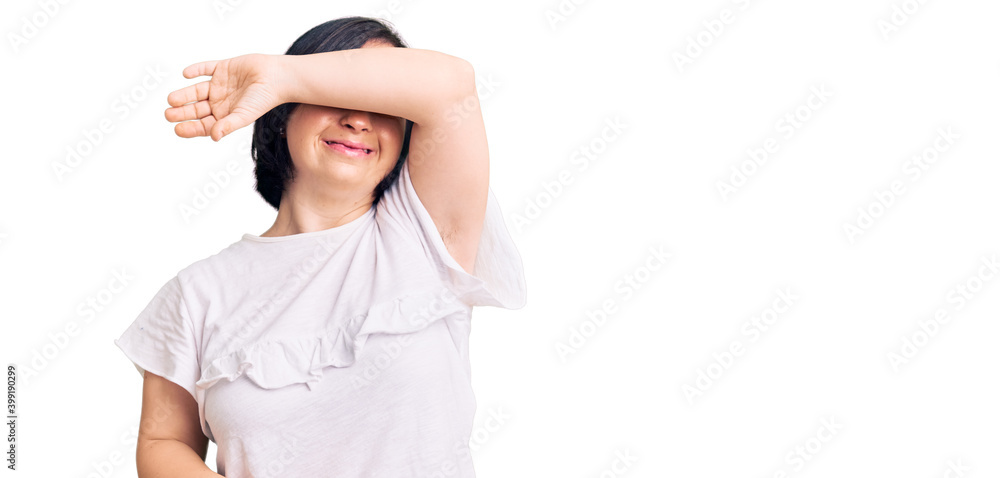 Brunette woman with down syndrome wearing casual white tshirt covering eyes with arm smiling cheerful and funny. blind concept. Brunette woman with down syndrome wearing casual white tshirt covering eyes with arm smiling cheerful and funny. blind concept.