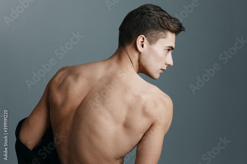Sexy man with a naked back looks to the side on a gray background rear view of a fitness sport