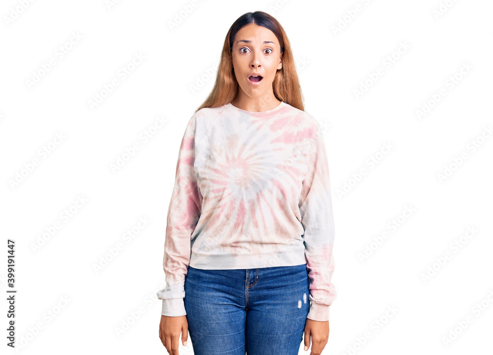 Fototapeta premium Beautiful young woman wearing casual tie dye sweatshirt scared and amazed with open mouth for surprise, disbelief face