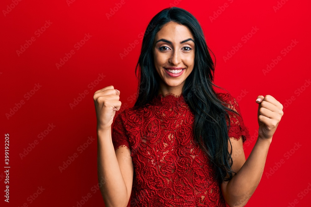 Beautiful hispanic woman wearing elegant clothes over red background screaming proud, celebrating victory and success very excited with raised arms Beautiful hispanic woman wearing elegant clothes over red background screaming proud, celebrating victory and success very excited with raised arms
