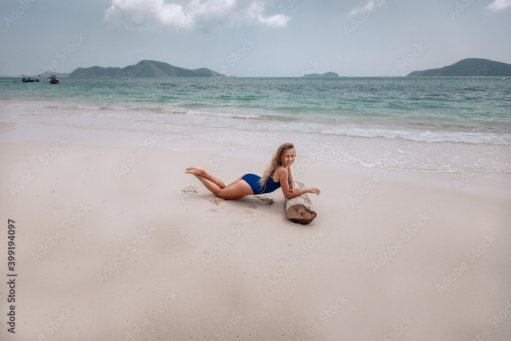 Young attractive blonde woman in a blue swimming suit lying on a sandy beach against the sea background. Summer vacation concept Young attractive blonde woman in a blue swimming suit lying on a sandy beach against the sea background. Summer vacation concept