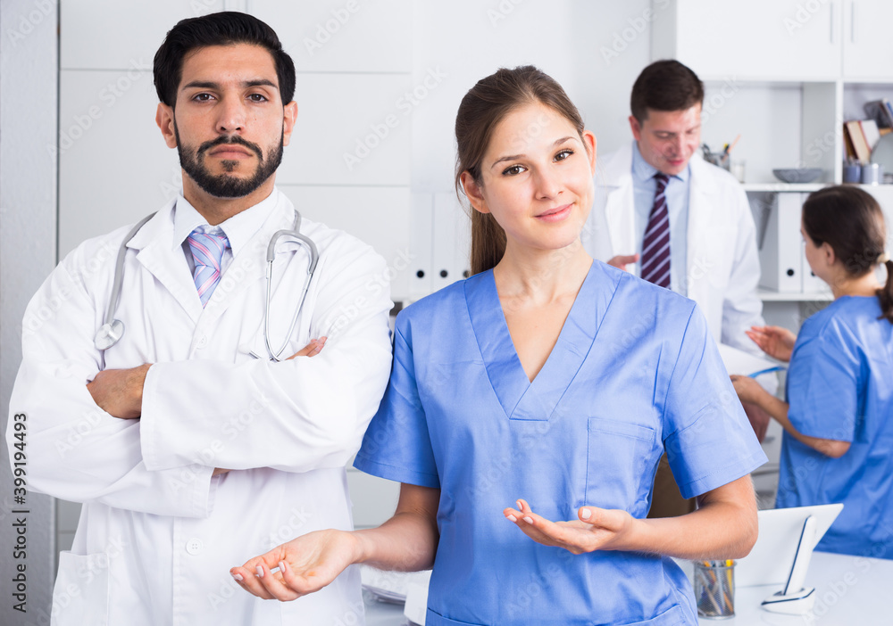 Fototapeta premium Portrait of young female doctor with male colleague inviting in clinic